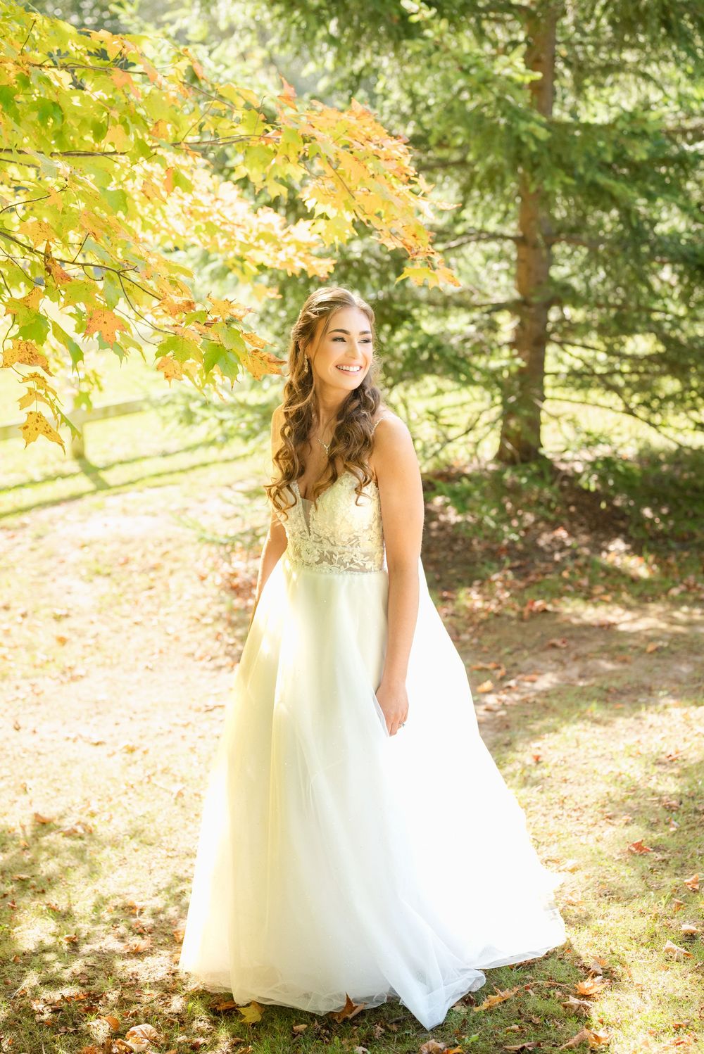 Bride in flowing white gown poses under golden autumn leaves.