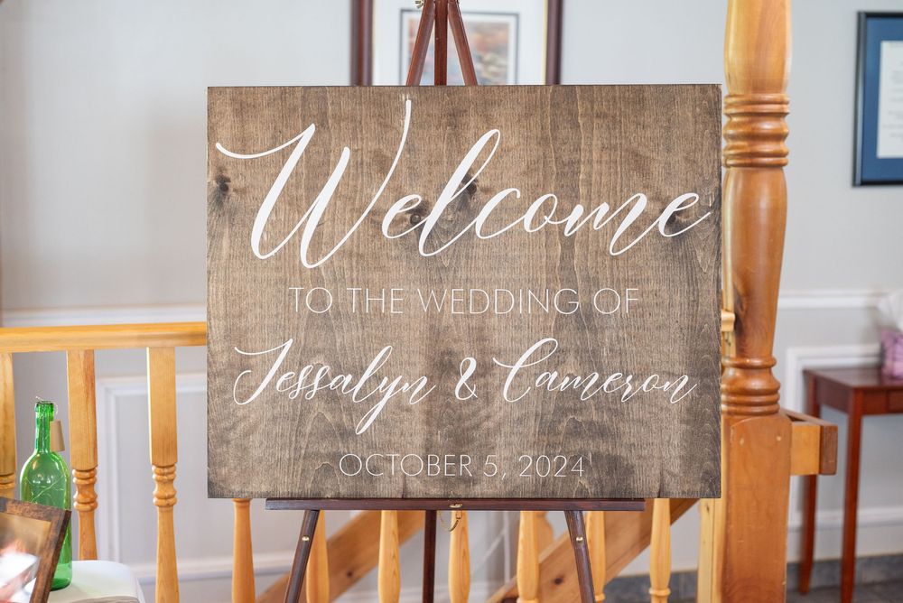 Rustic wooden welcome sign for a wedding with white calligraphy text on natural wood background.