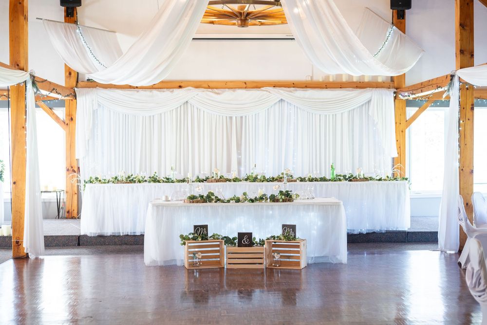 Rustic barn wedding reception venue with white draping, wooden beams, and elegant head table setup.