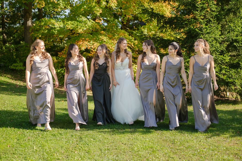 Bridal party in coordinated gray dresses walking on grass with fall trees in background.