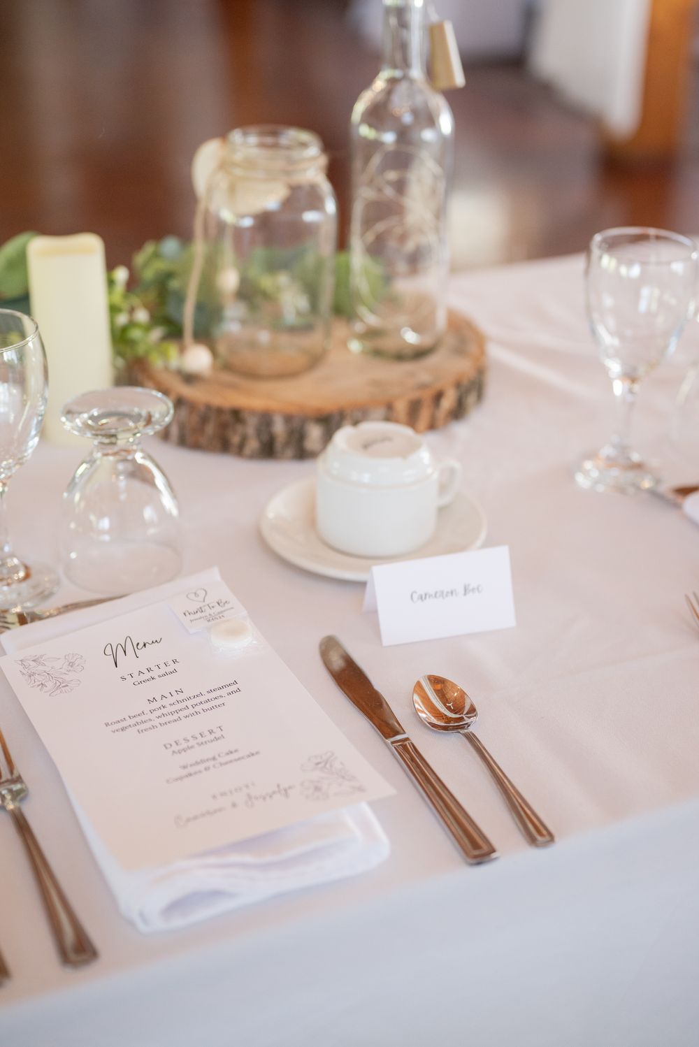 Rustic wedding table setting with menu card, glassware, and wooden slice centerpiece.