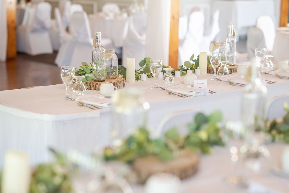 An elegant wedding reception table set with candles, greenery and neutral decor in a bright indoor venue.