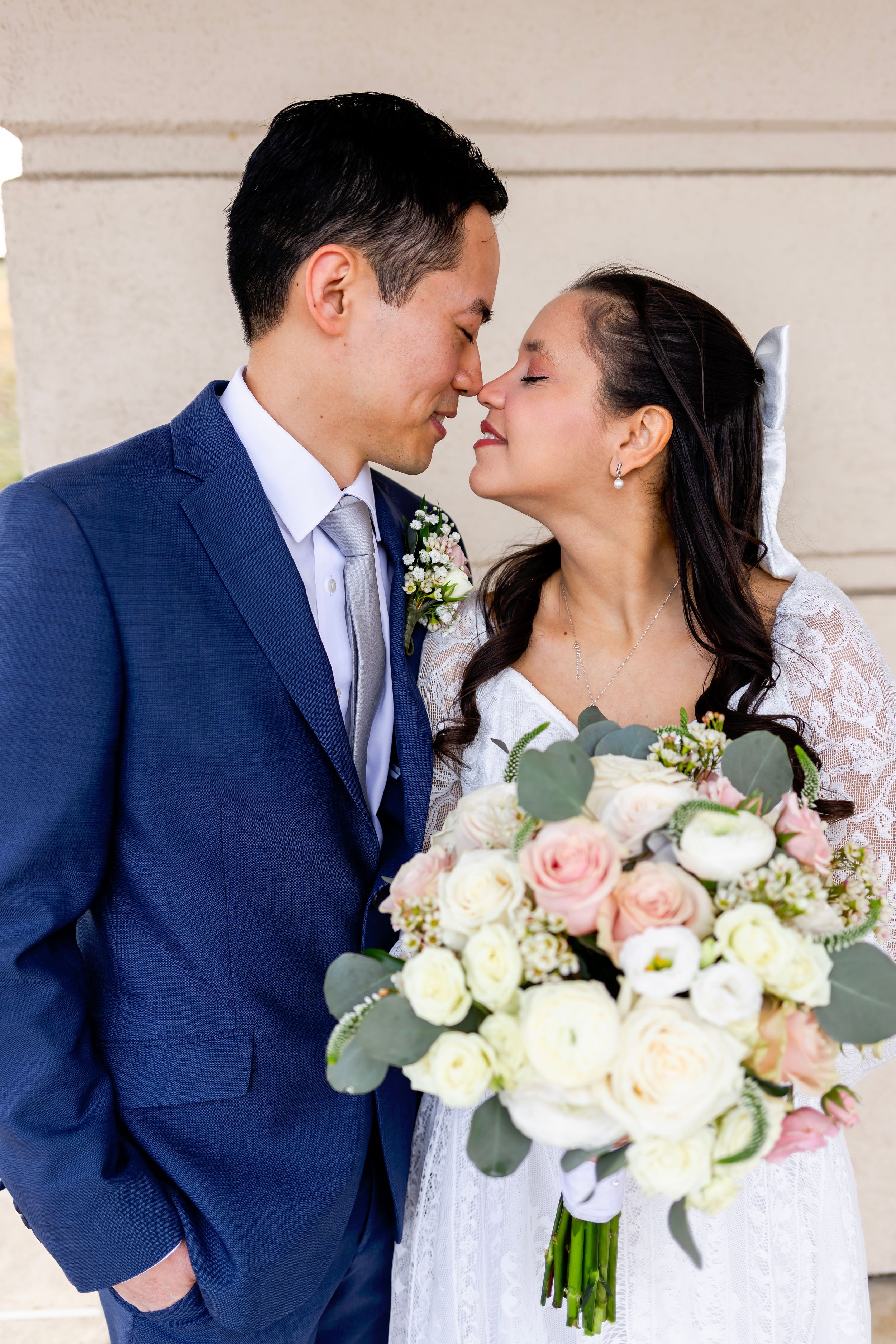 Couple shares tender moment on wedding day with bride holding elegant bouquet of blush roses and eucalyptus.