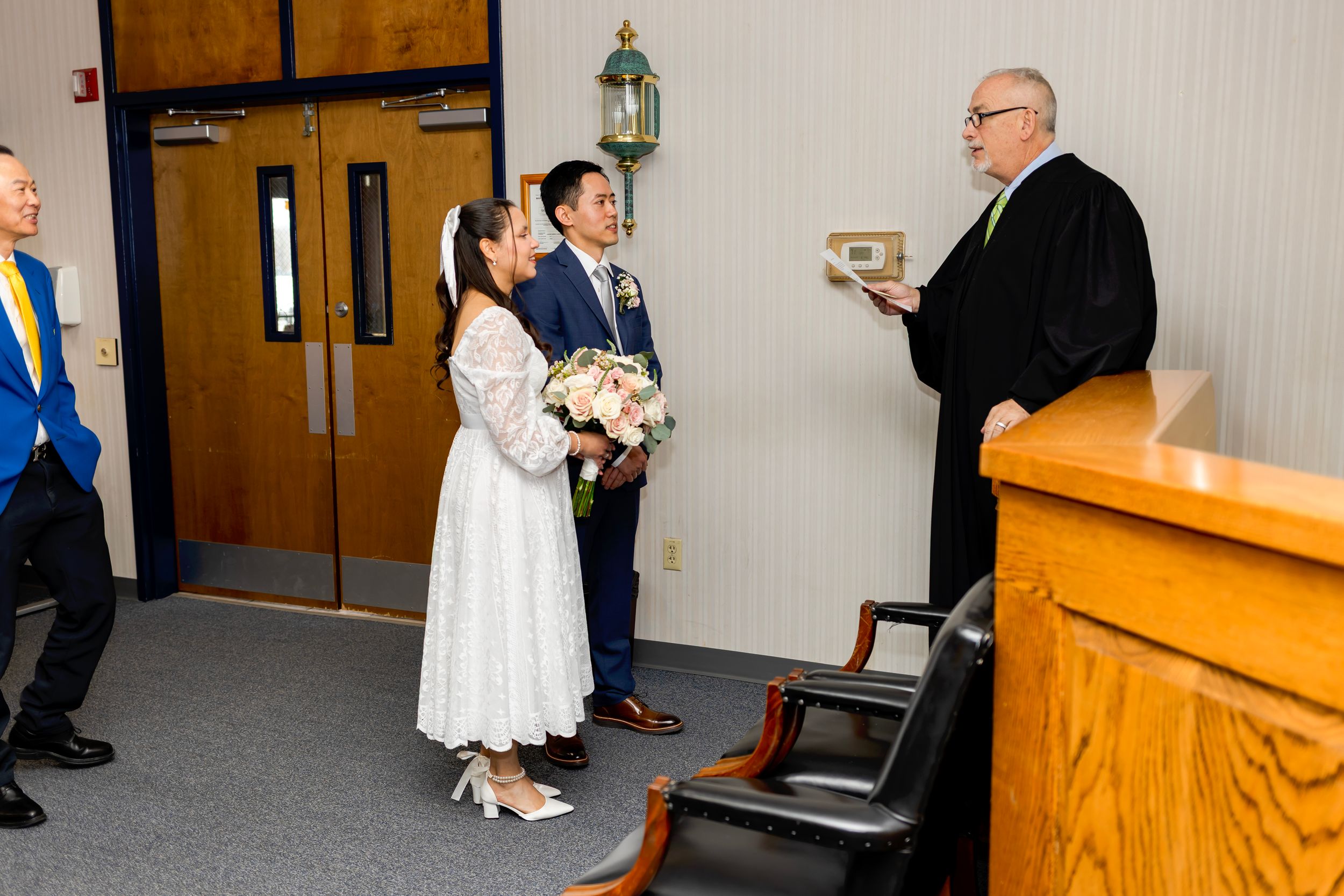 A couple stands at a podium with an officiant during an intimate indoor wedding ceremony.