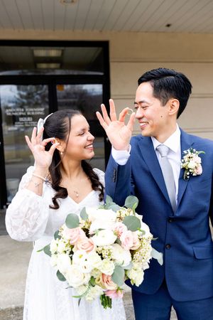 A joyful couple in wedding attire share a candid moment while holding a blush and white floral bouquet with eucalyptus.