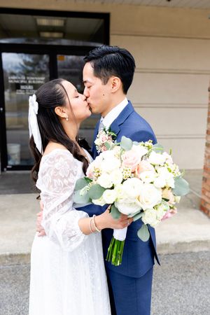 A romantic wedding couple share a kiss while holding a beautiful bouquet of white flowers and eucalyptus.