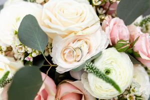 Wedding rings nestled in cream and pink roses with eucalyptus leaves in an elegant floral arrangement.