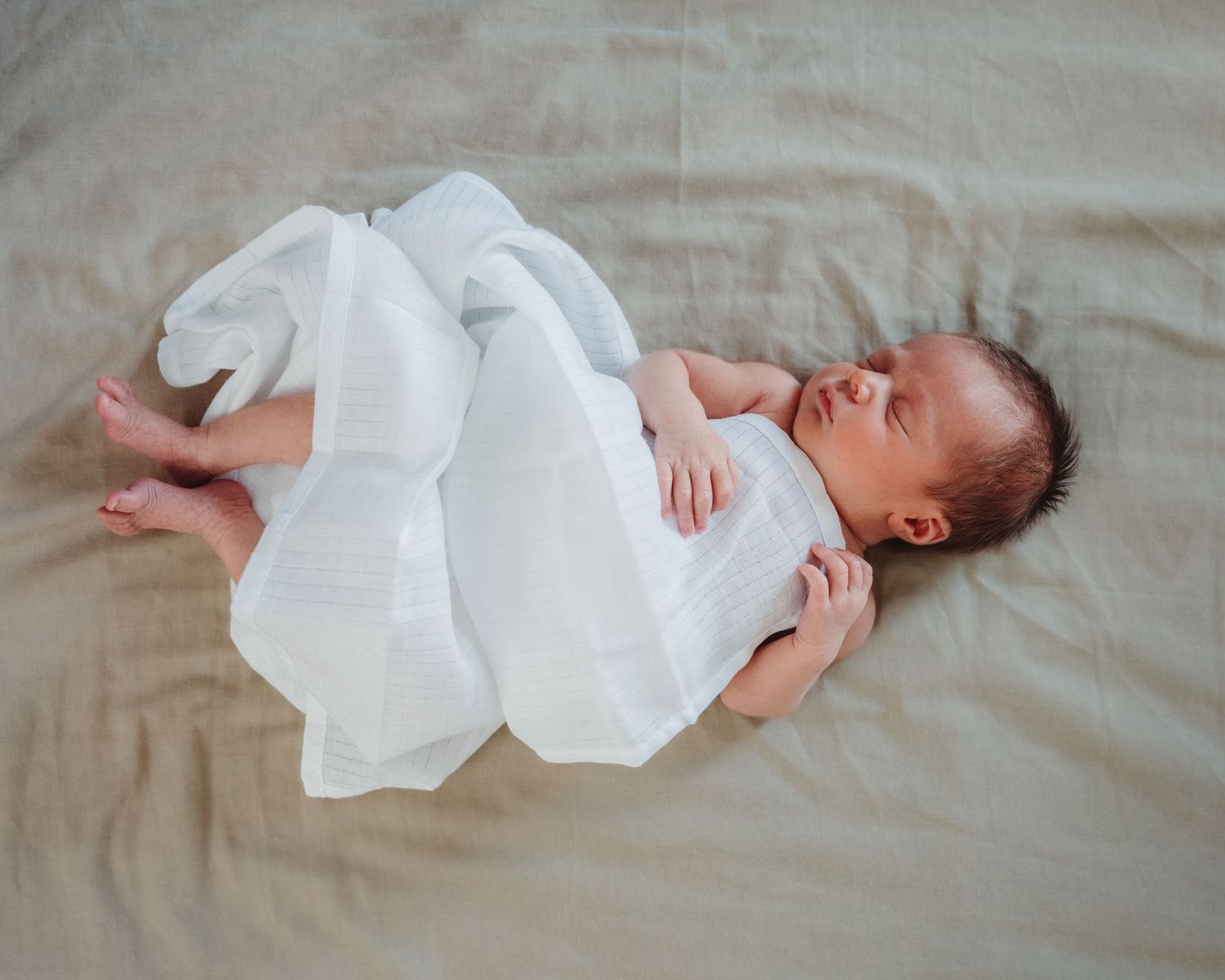 Newborn baby wearing white onesie lying on beige blanket.
