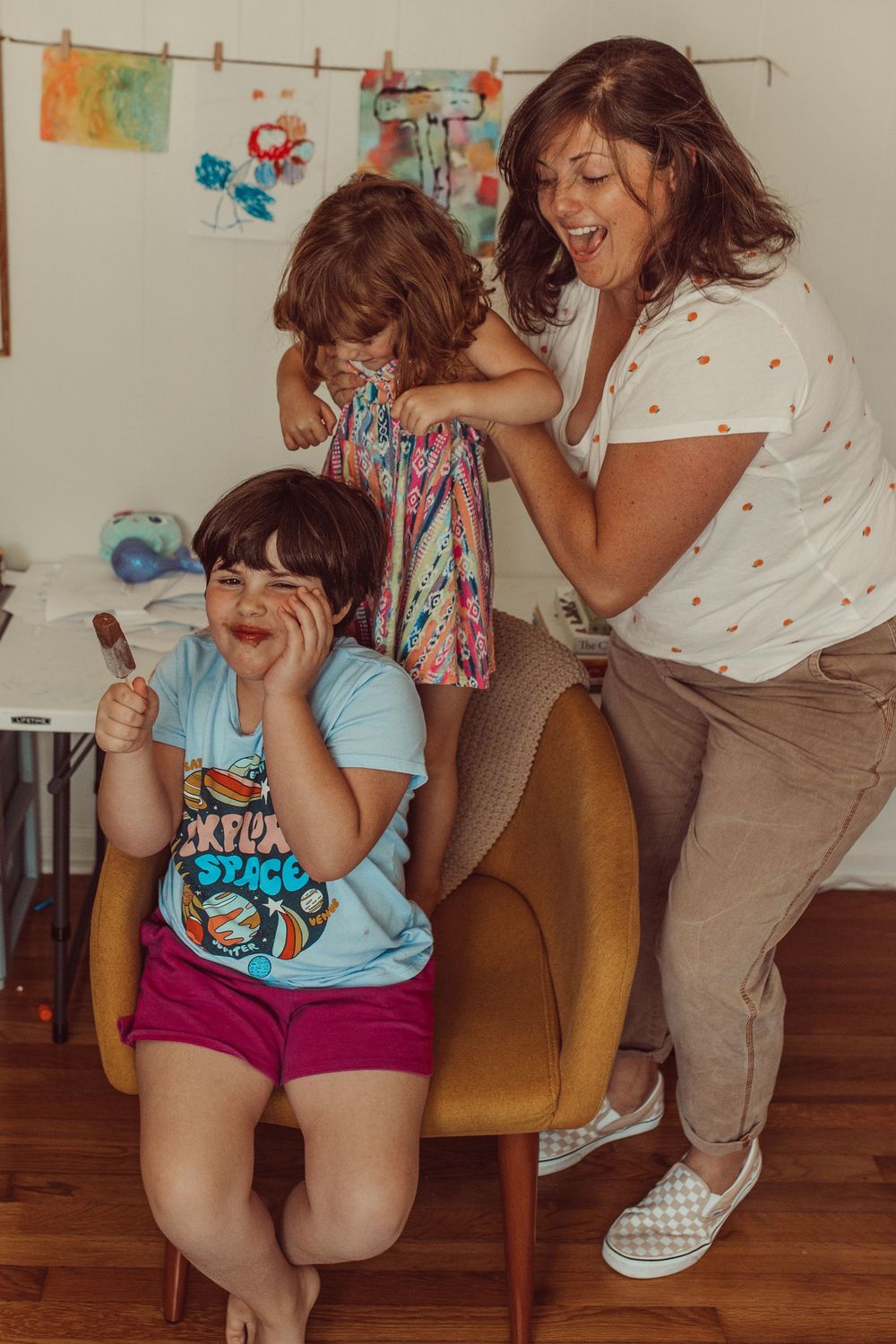 A joyful candid moment of people laughing together in a casual indoor setting with children's artwork displayed behind them.