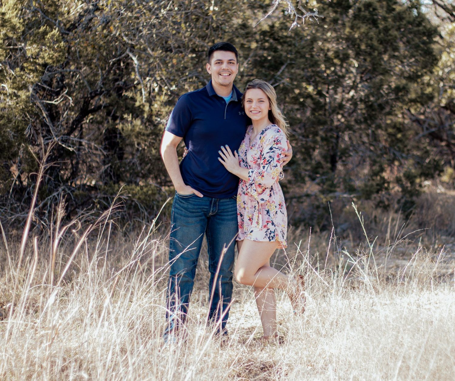 Two people stand together overlooking a scenic desert landscape with rolling hills and scrubland on a clear day.