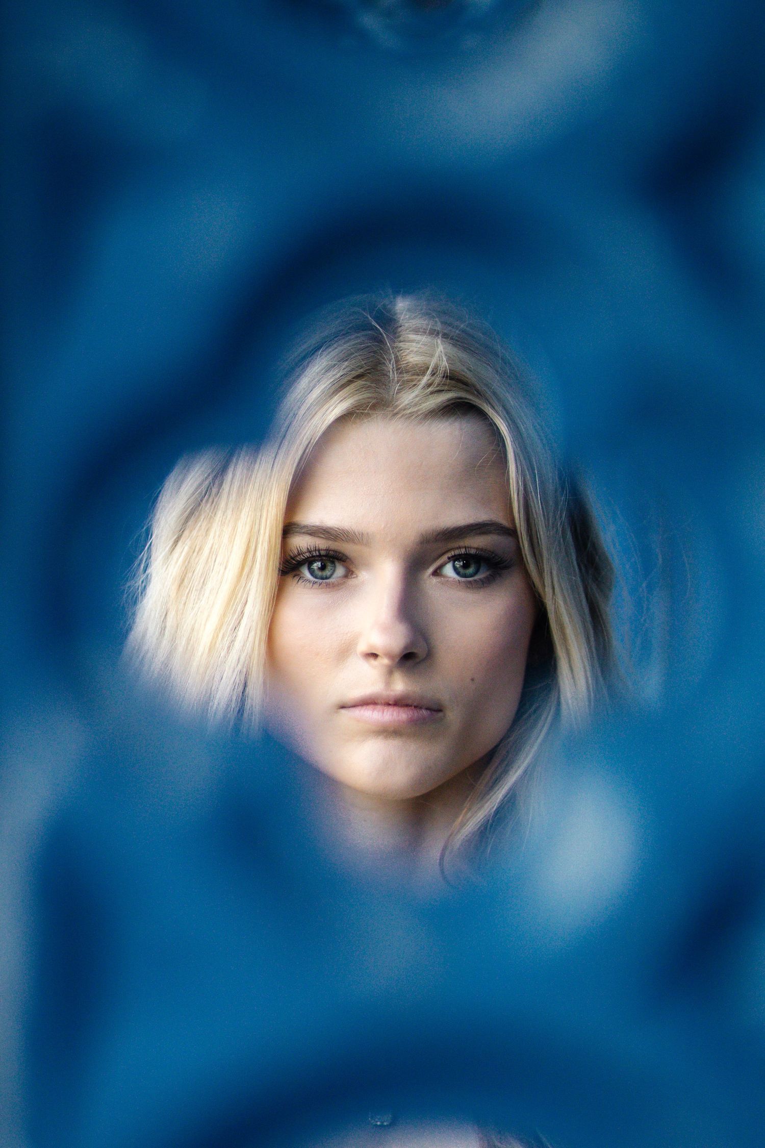 Artistic portrait through blue bokeh effects showing a close-up against a deep blue background.