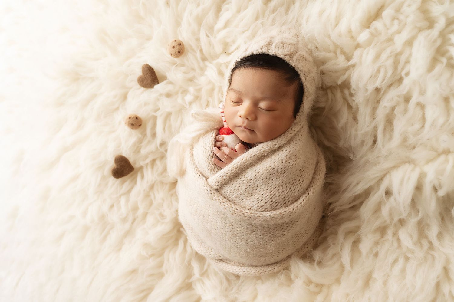 Sleeping newborn wrapped in beige blanket on soft white fur backdrop.