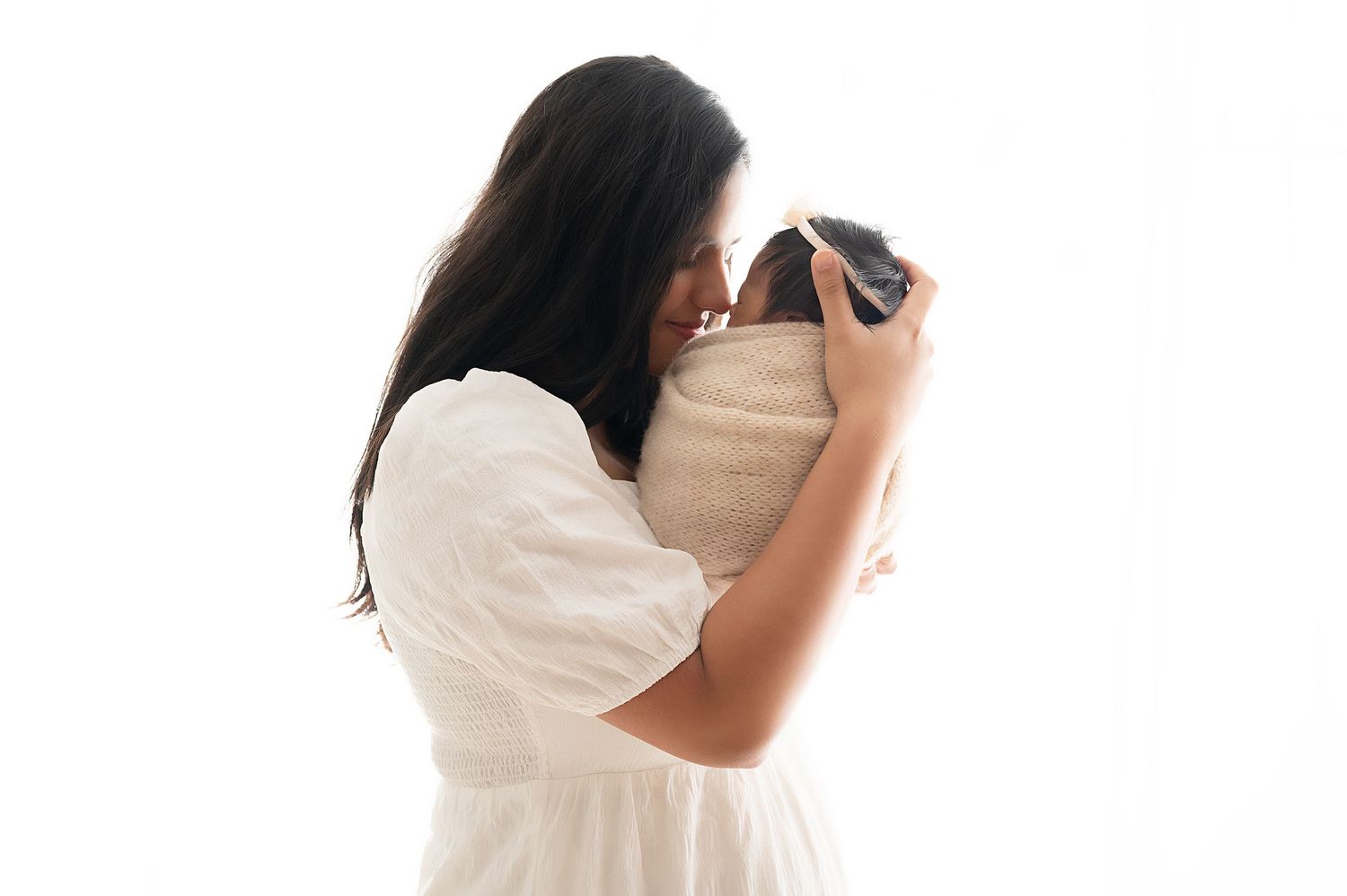 Tender parental moment captured with baby against white backdrop.