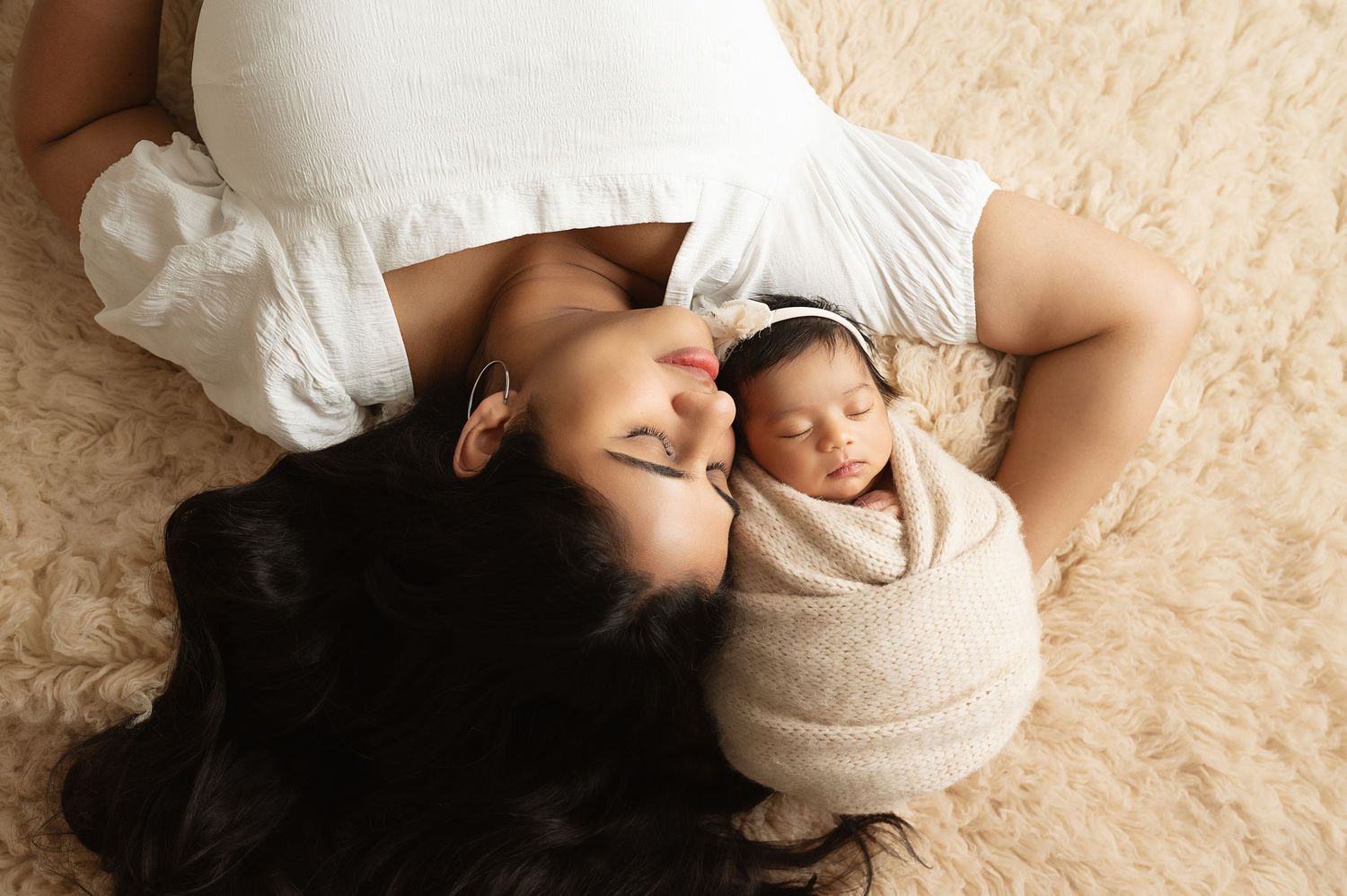 Family lying together on beige carpet in casual white outfits during intimate photo shoot.