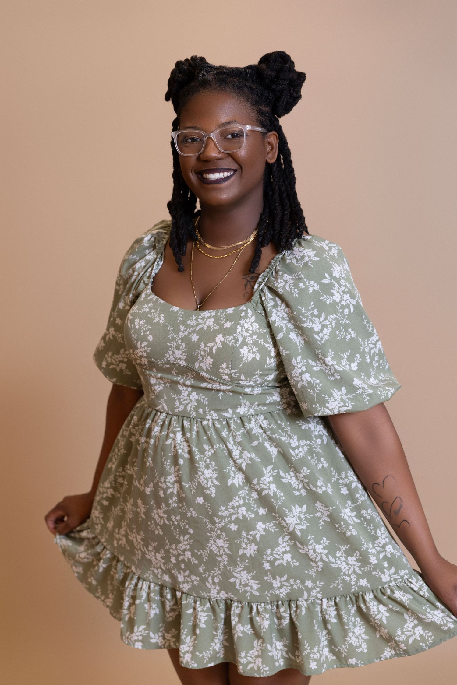 Portrait of person in floral print dress with glasses against neutral background.