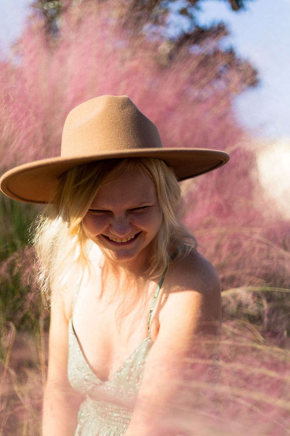A joyful moment captured in a white dress and tan hat among pink muhly grass during golden hour.