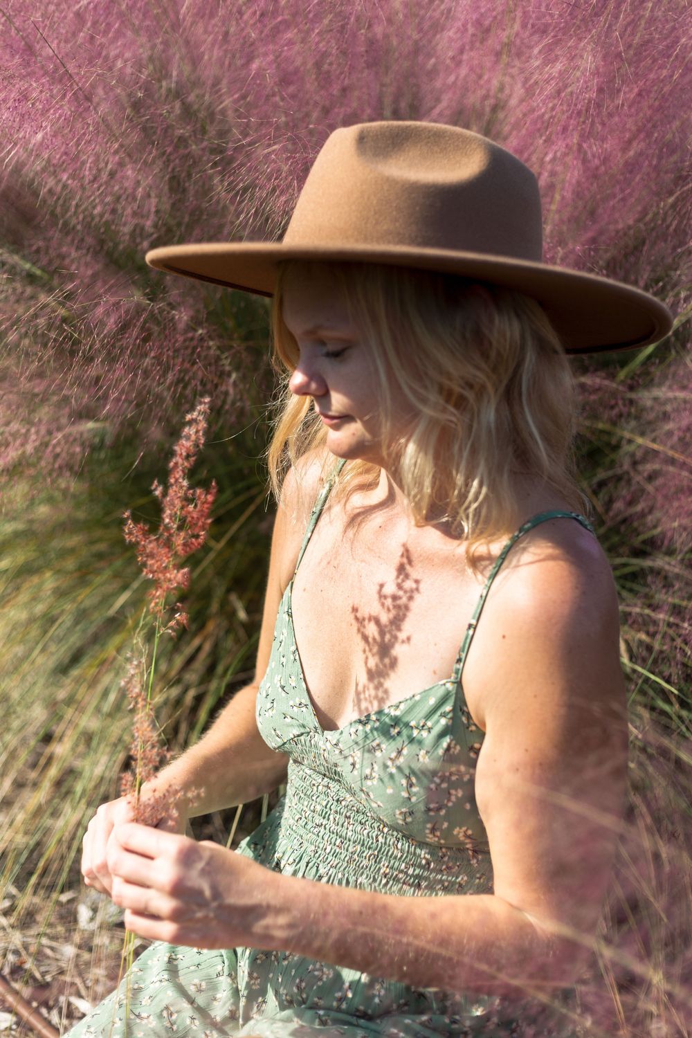 A person in a green sundress and brown hat stands among pink wildflowers on a dreamy summer day.