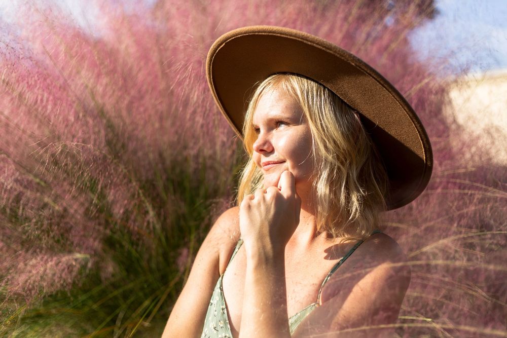 Dreamy portrait with sun hat against pink flowering grass in golden sunlight.