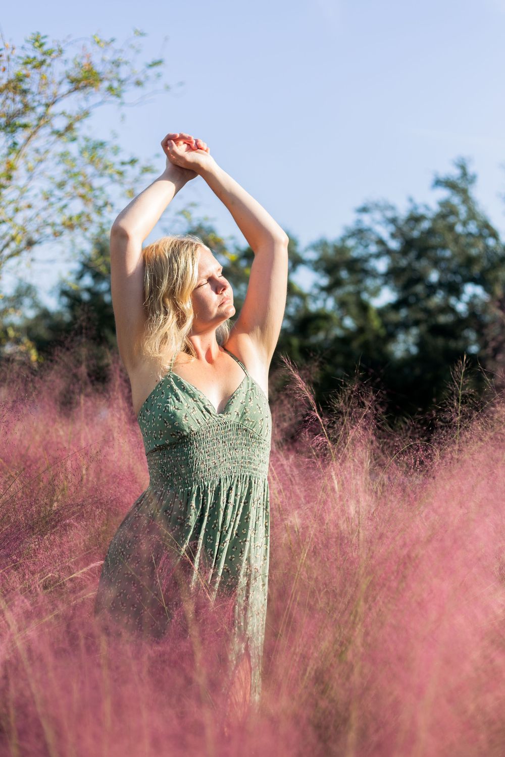 A figure in a green sundress stands gracefully among pink wildflowers on a sunny summer day.