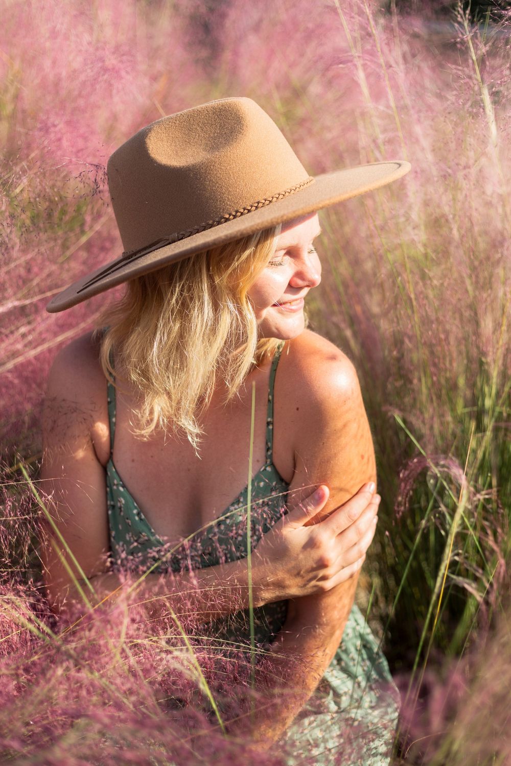 Brown felt cowboy hat stands out against soft pink muhly grass during golden hour in a dreamy outdoor portrait.
