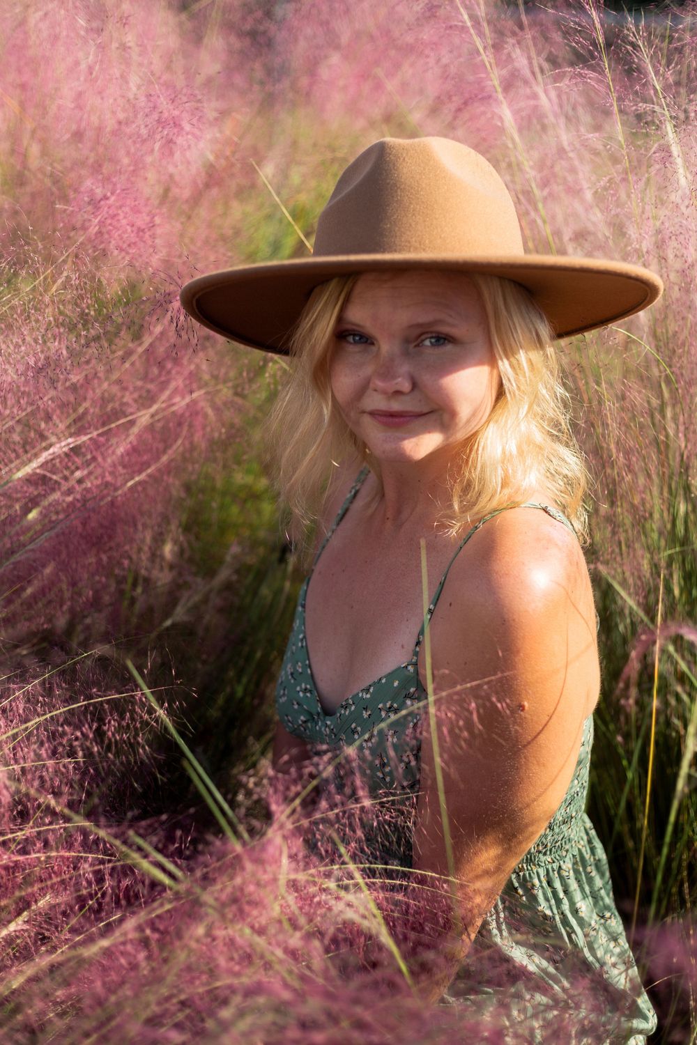 A brown wide-brimmed hat stands out against pink muhly grass on a sunny day, creating a dreamy outdoor portrait.
