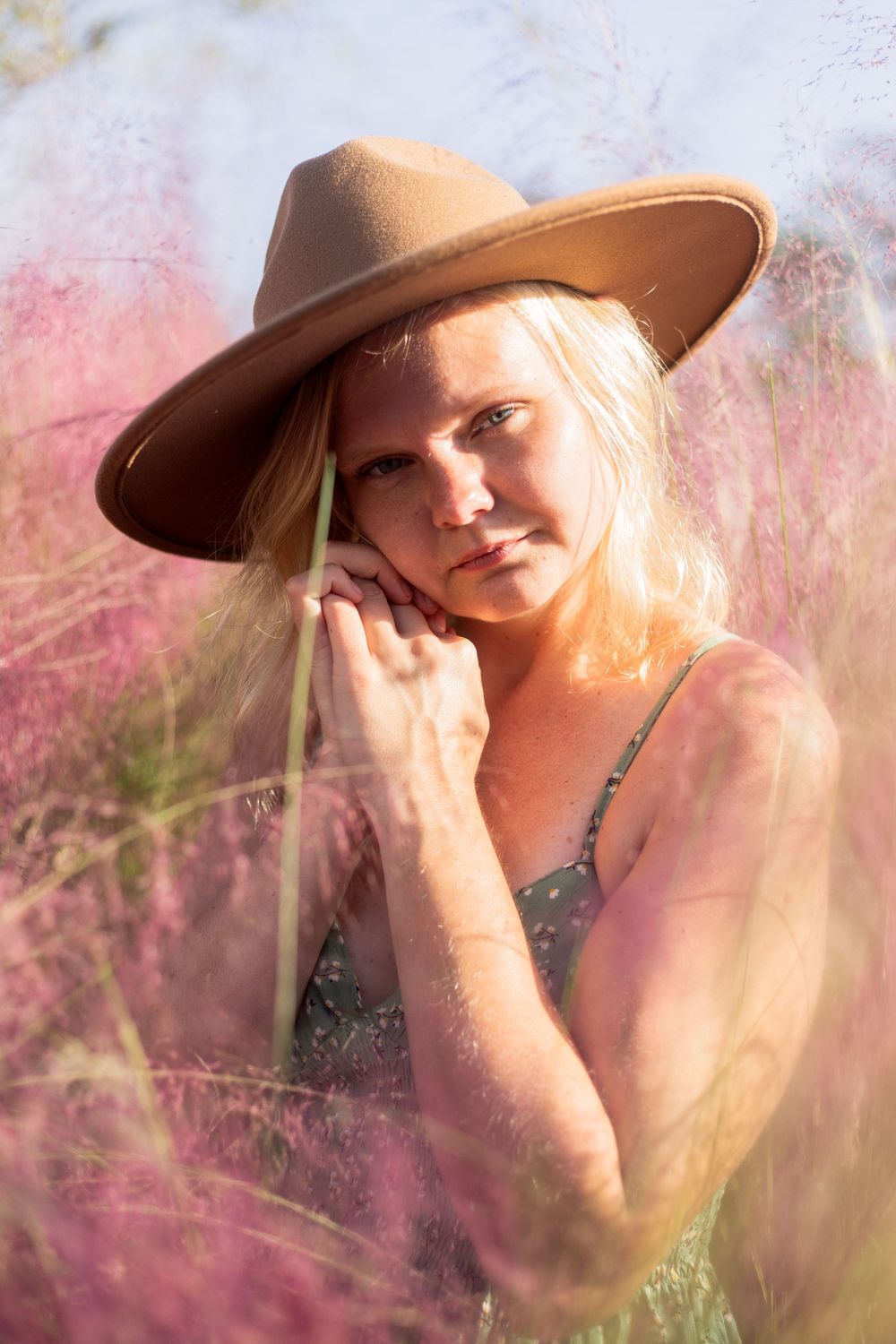A dreamy outdoor portrait in a field of pink flowers with warm sunlight and a tan wide-brimmed hat.
