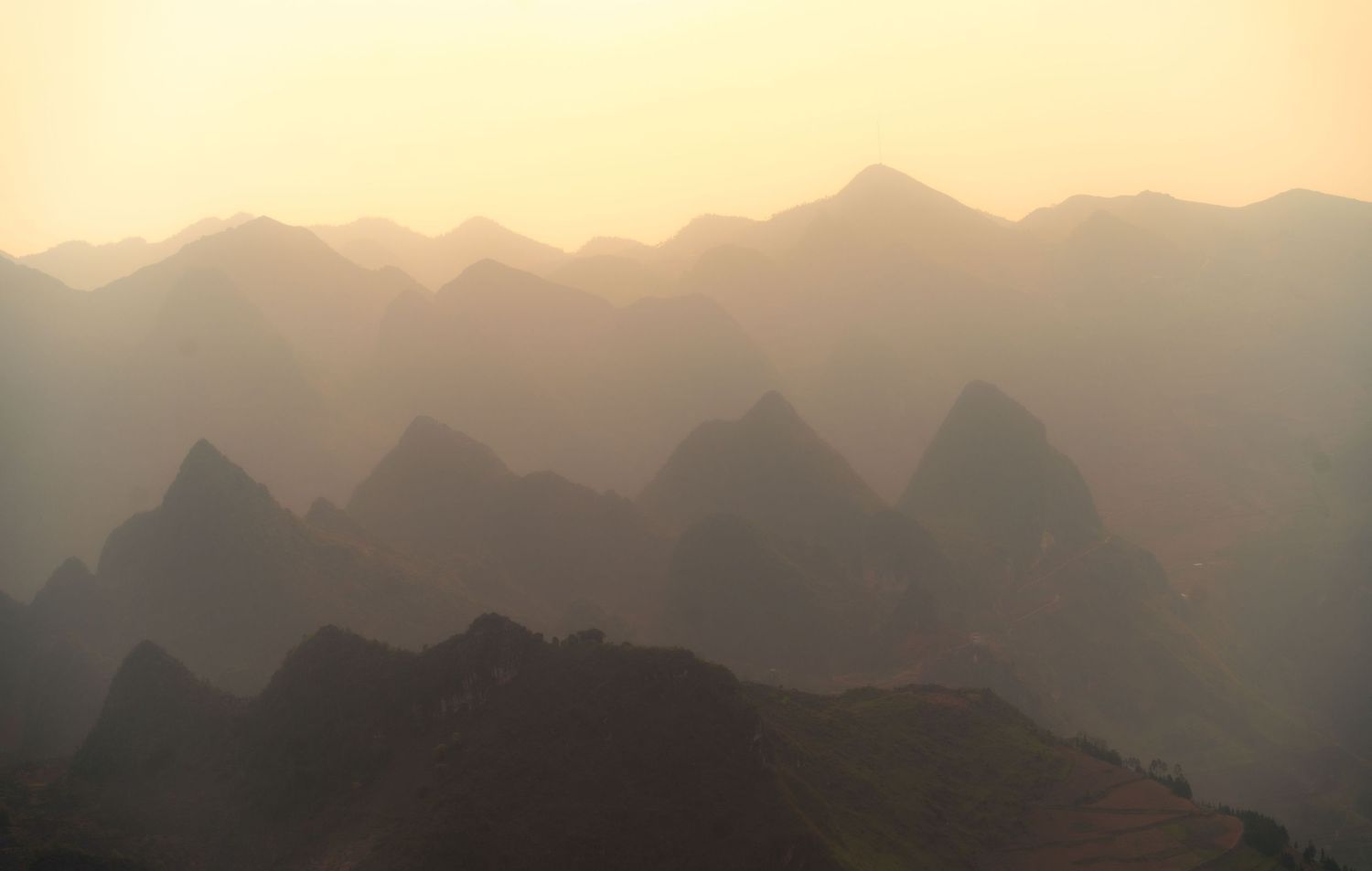 Misty mountain ranges layered in golden light during sunset.