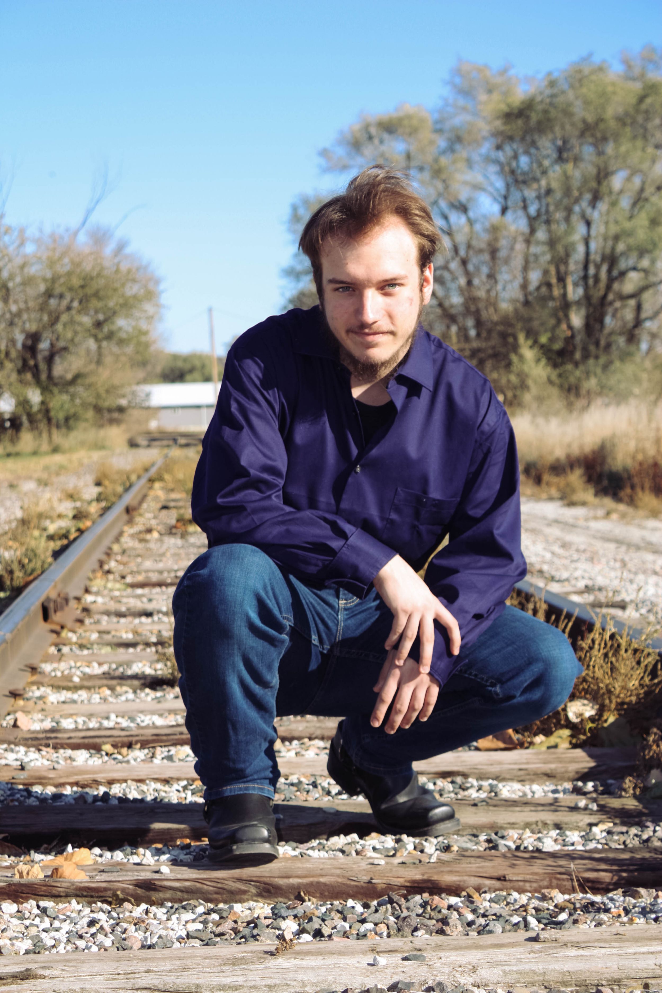 Figure crouching on train tracks wearing dark blue shirt and jeans.