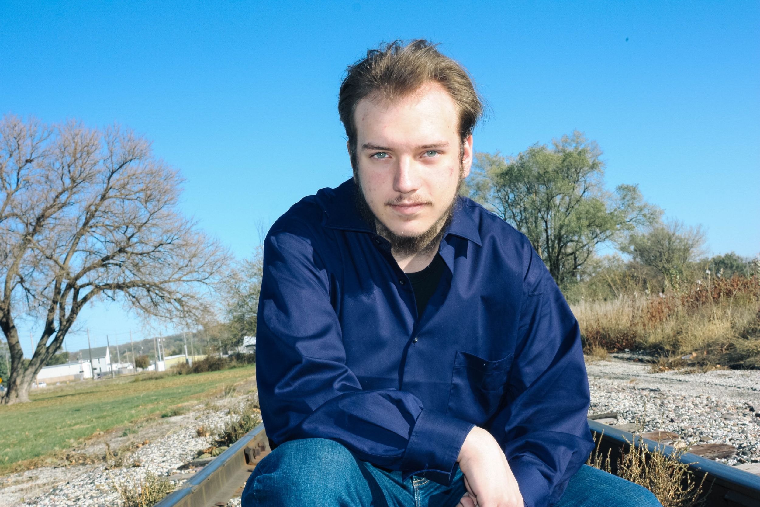 Person in navy blue shirt posing on railroad tracks during daytime photoshoot.