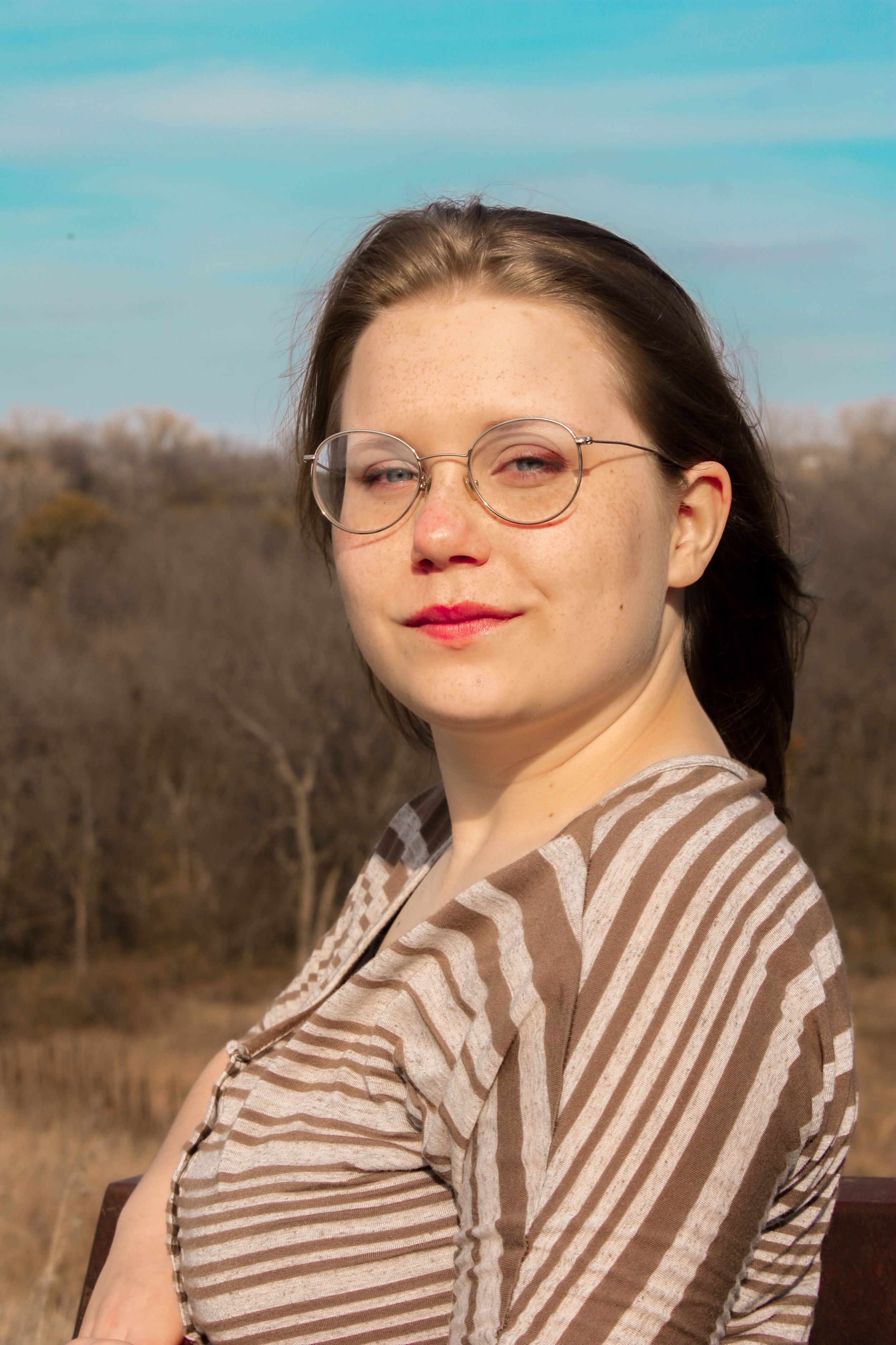 A portrait against blue sky wearing a brown striped collared shirt.