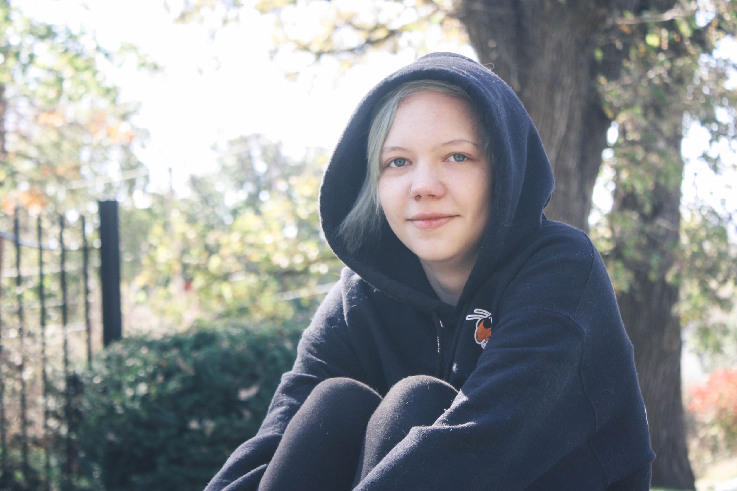 Person wearing black hooded sweatshirt outdoors on sunny autumn day.