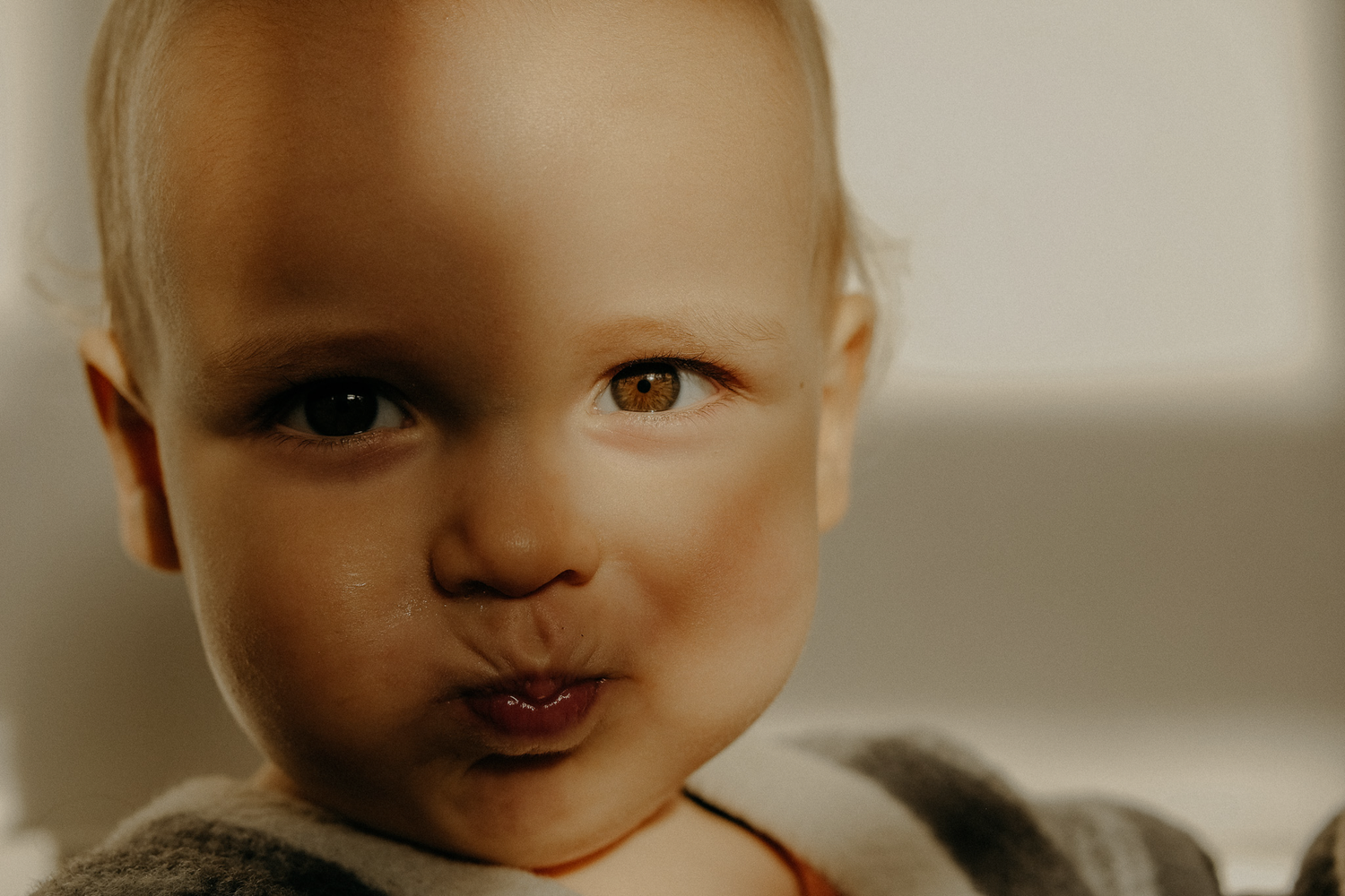 Baby with bright eyes making a playful face in soft window light — candid infant portrait full of personality.