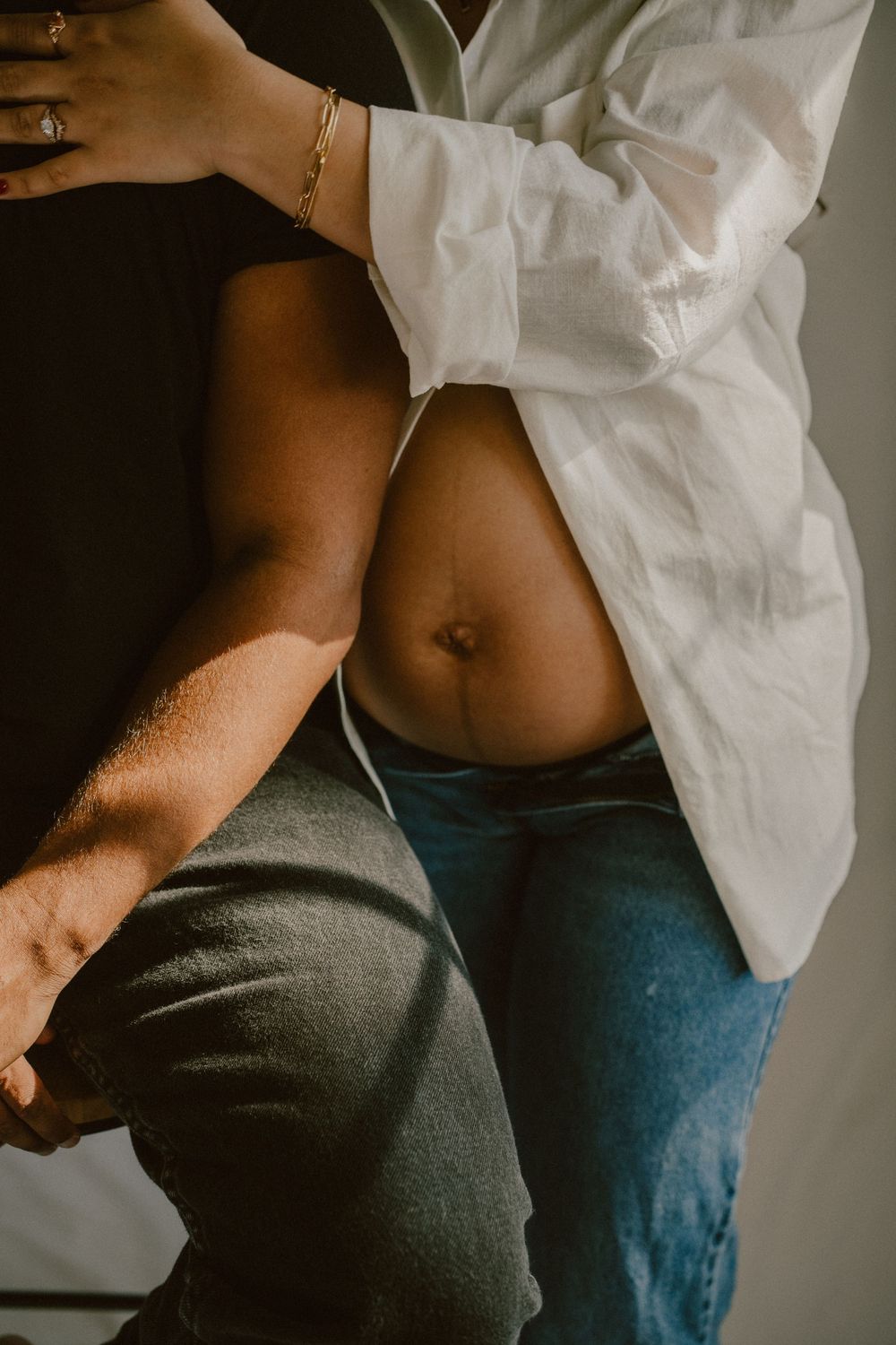 Intimate maternity photo showing bare pregnant belly with white shirt and jeans.