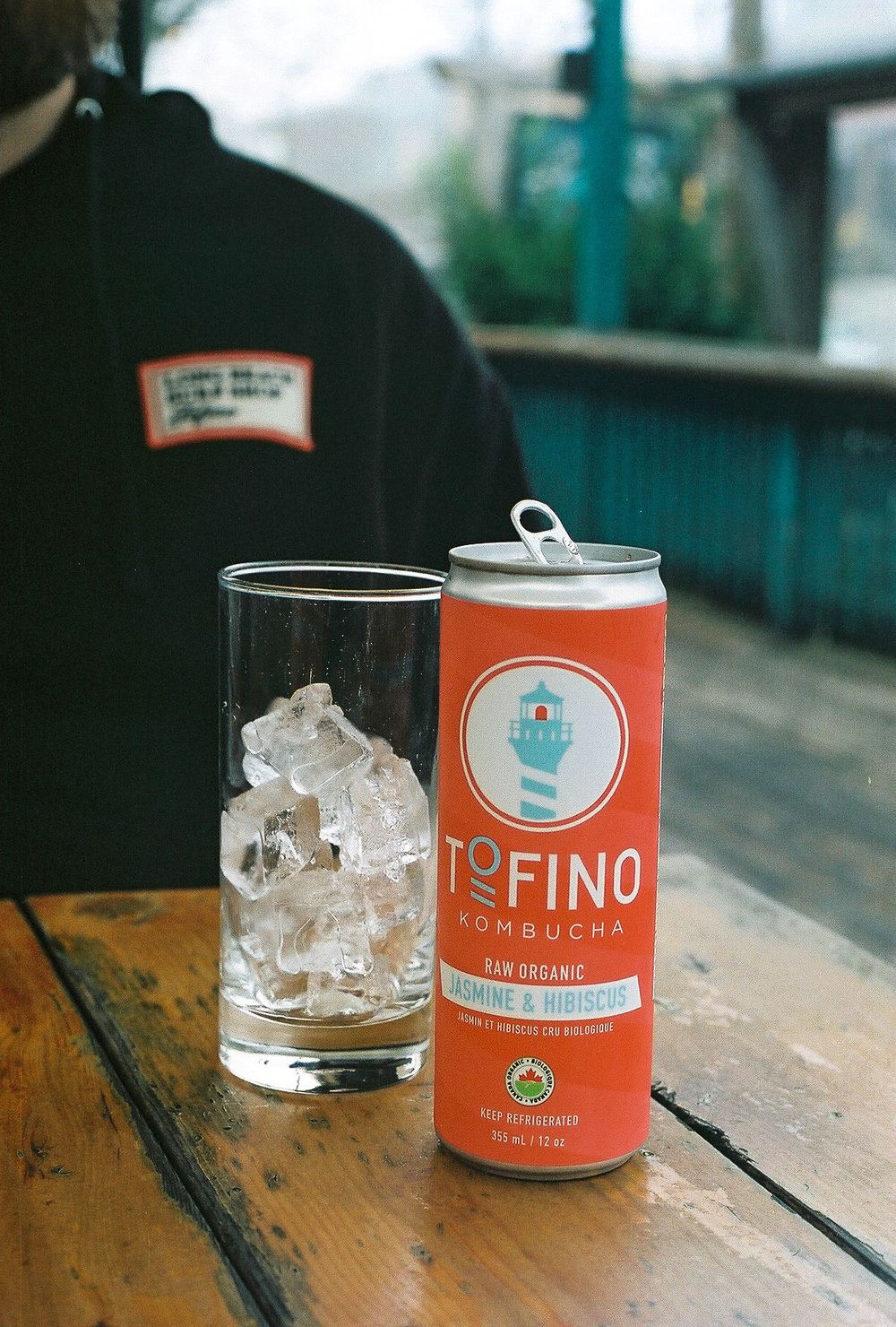 A can of Tofino kombucha next to a glass filled with ice on a wooden table.