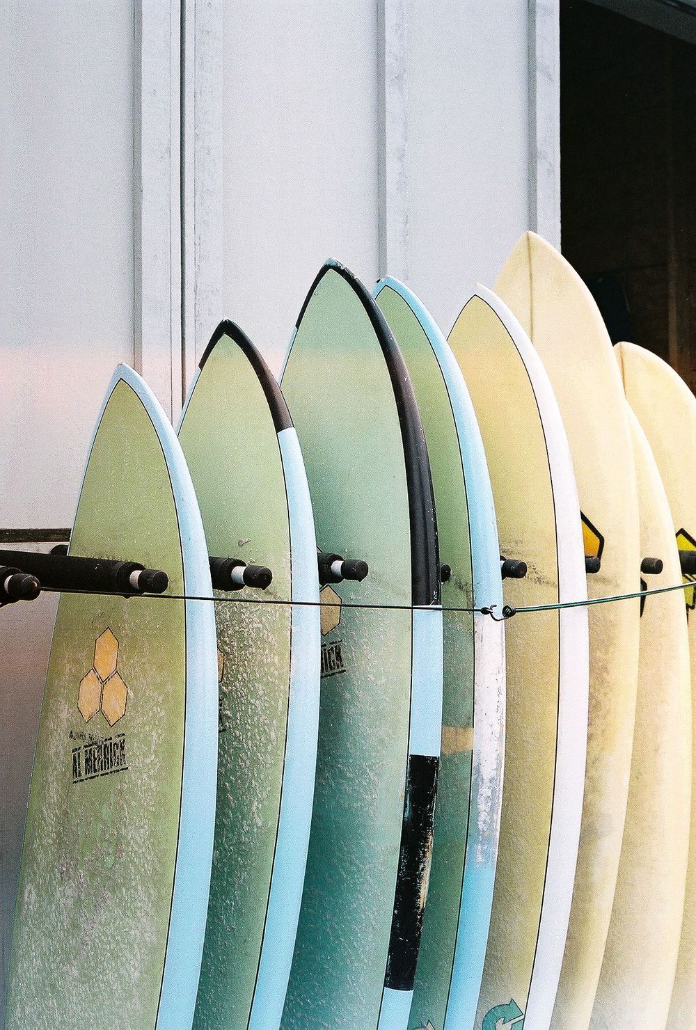 A row of pastel-colored surfboards arranged vertically against a white wall.