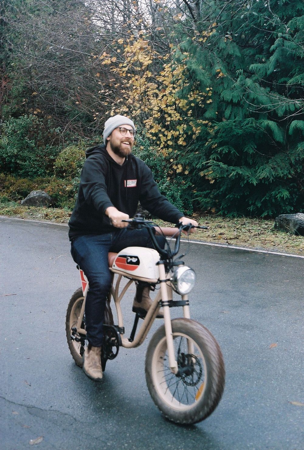 Person riding a custom motorcycle on a curved road through autumn trees.