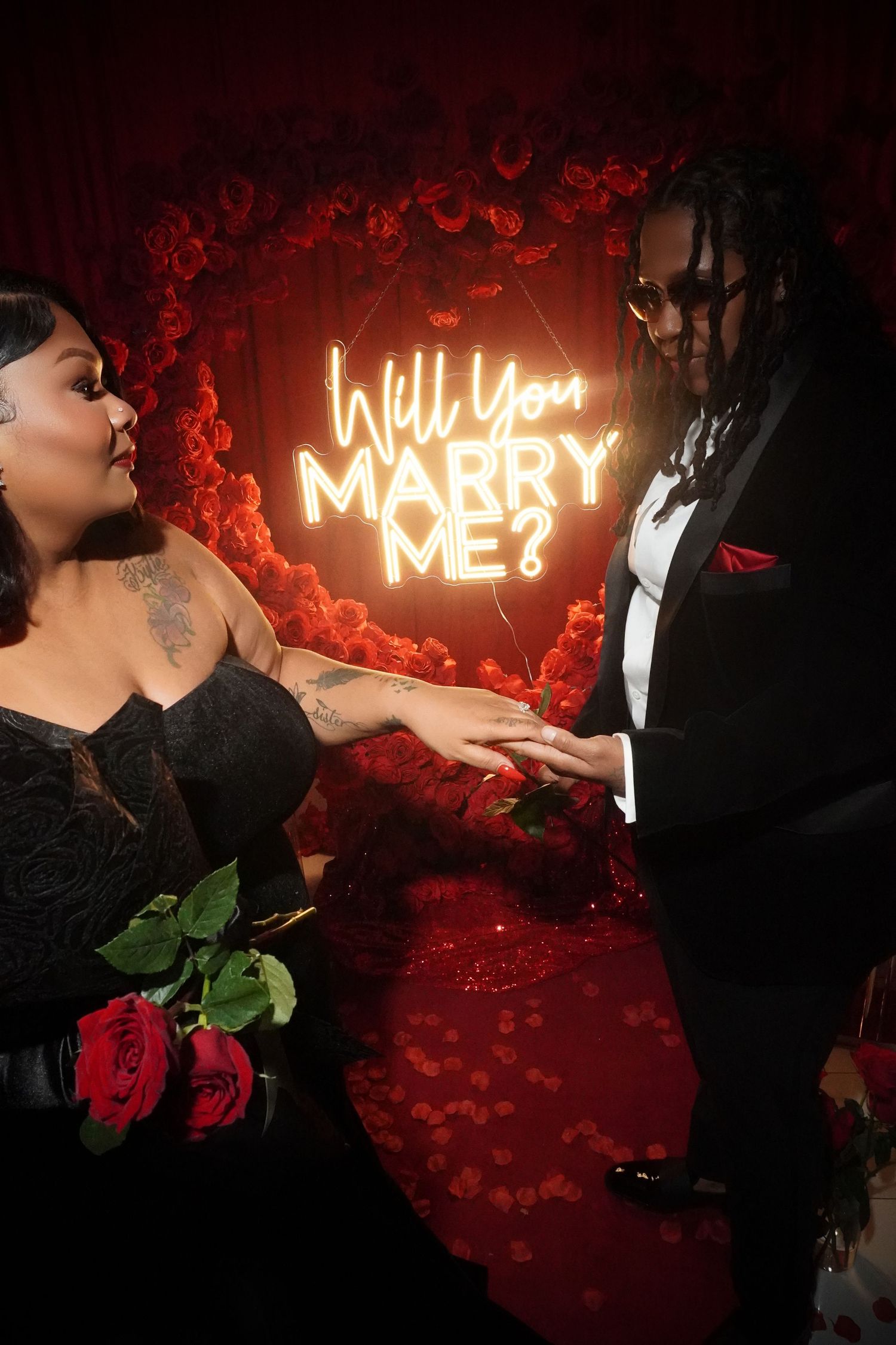 A romantic proposal scene with roses and a glowing 'Will You Marry Me' neon sign in the background.