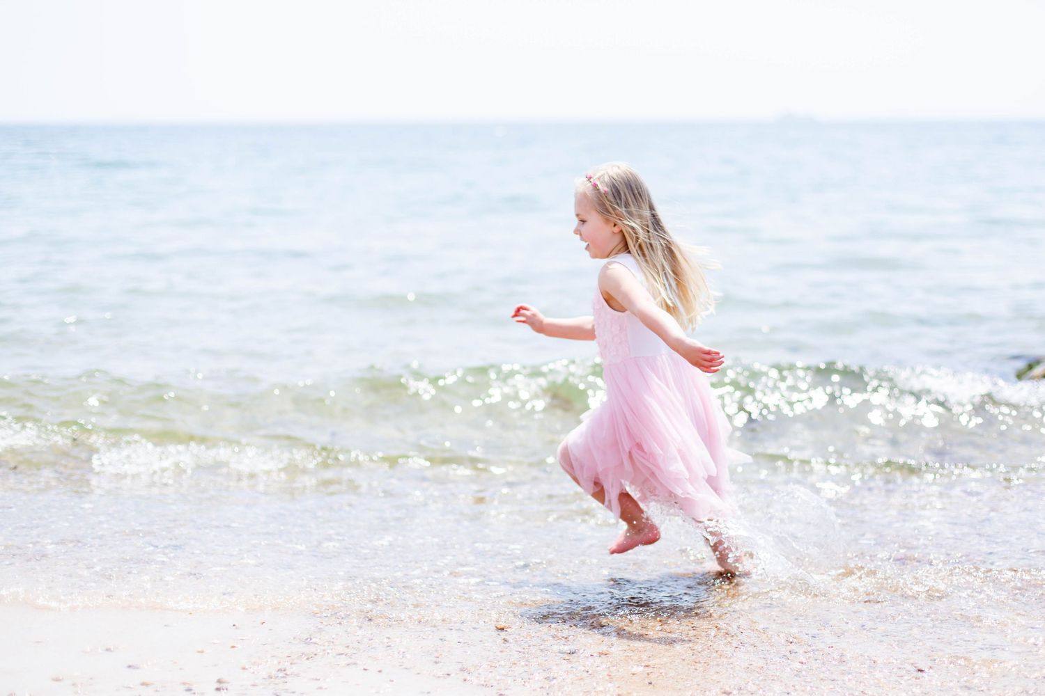 Young girl in pink dress playing and splashing in ocean waves at the beach.