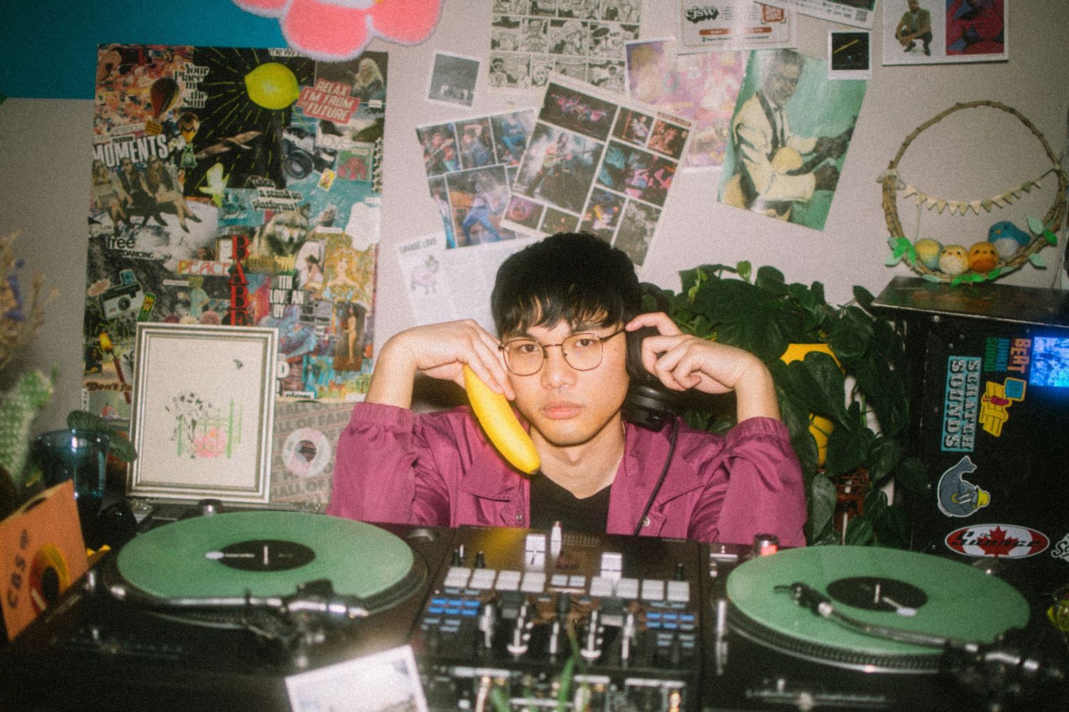 DJ setup with turntables and mixer in bedroom decorated with photos and posters on wall.
