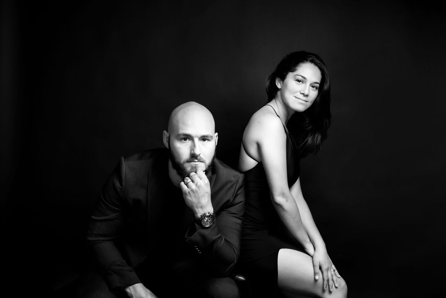 Editorial-style black and white studio portrait of a couple in sophisticated outfits, full of emotion and presence.