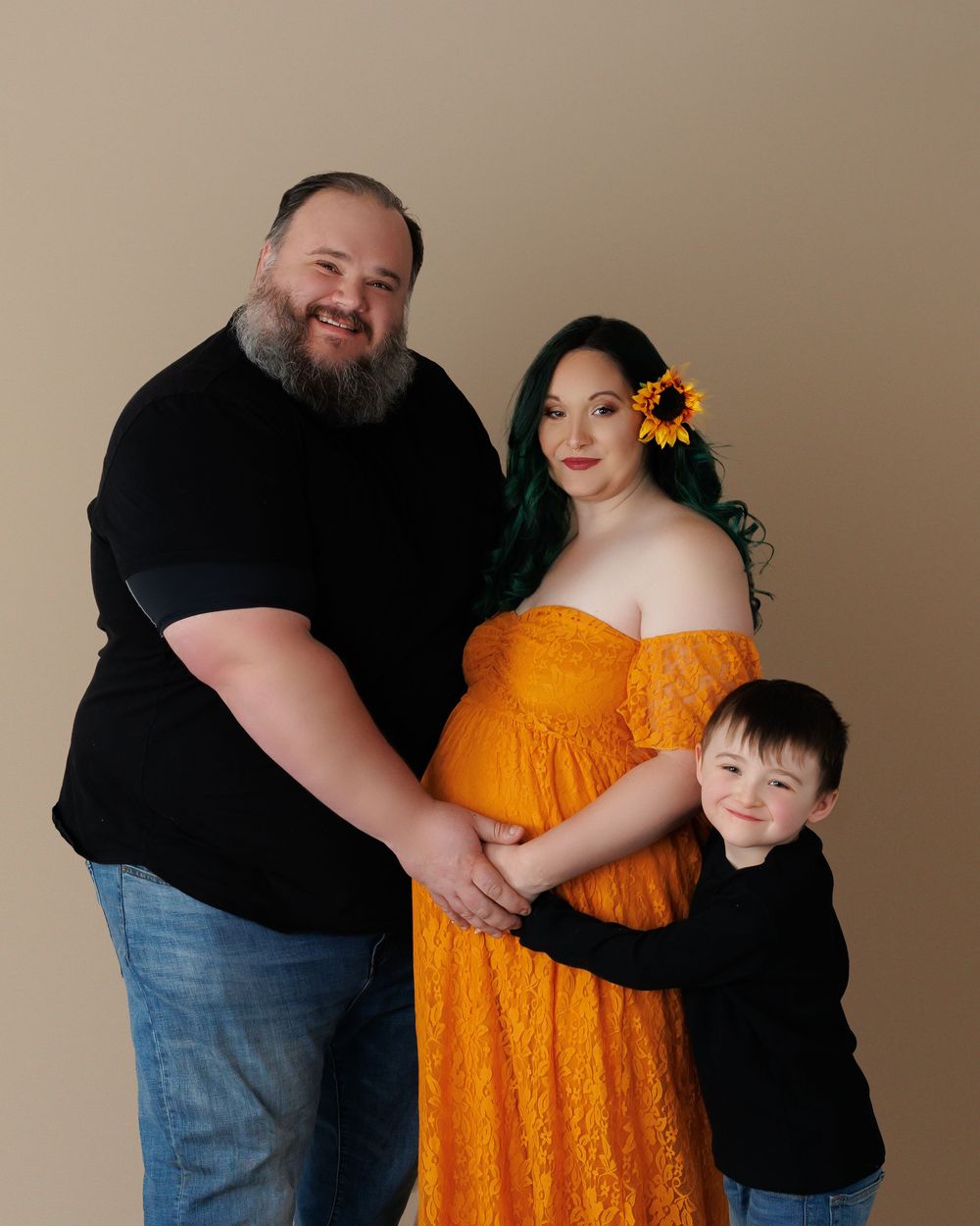 Family portrait featuring a maternity shoot with a woman in orange dress, joined by two others on a neutral background.