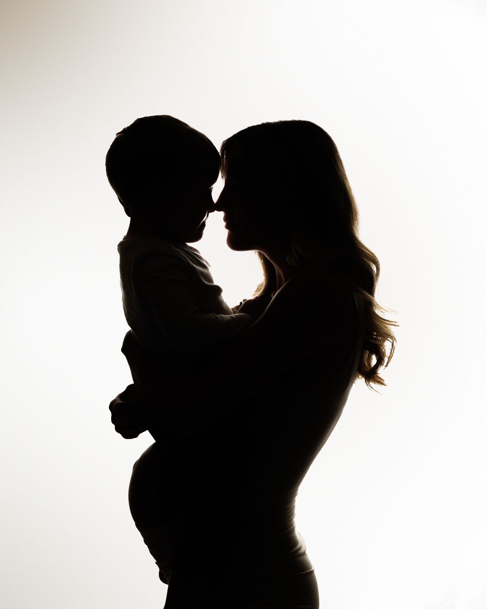 Silhouette portrait against white background shows intimate moment between parent and child in tender embrace.