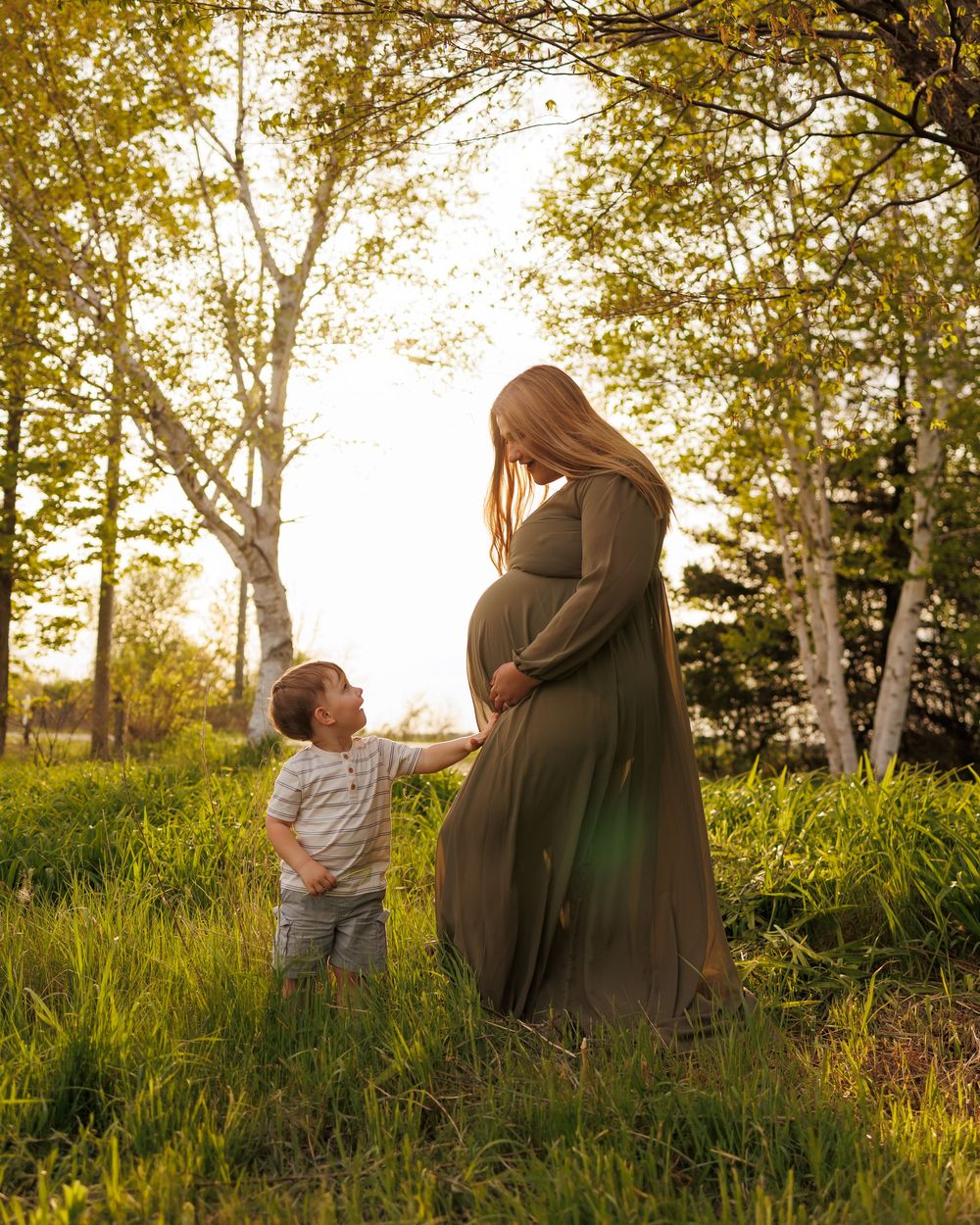 Two figures share a tender moment in a sunlit meadow during golden hour as tall grass and trees sway in the breeze.