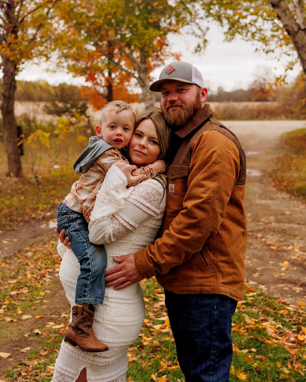 A family shares tender moments together on a fall day with autumn leaves scattered on the ground.