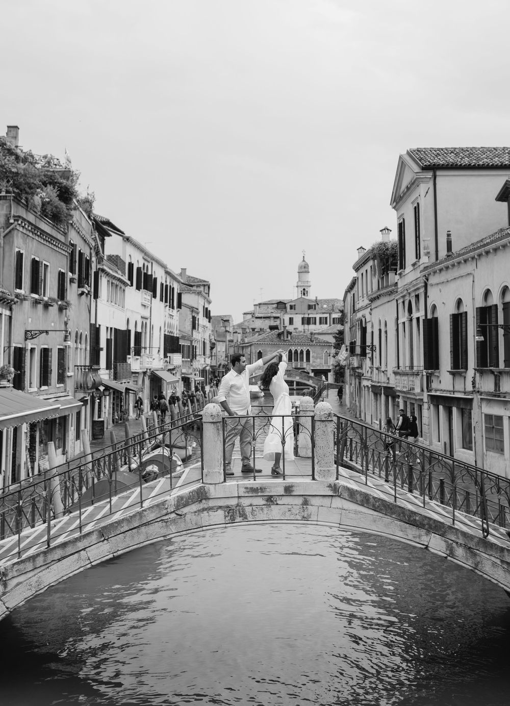 A black and white photograph of a scenic Venetian canal with a bridge and historic buildings lining both sides.