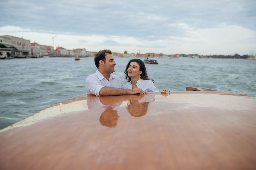 Couple enjoying romantic wooden boat ride through Venice's lagoon on cloudy day.