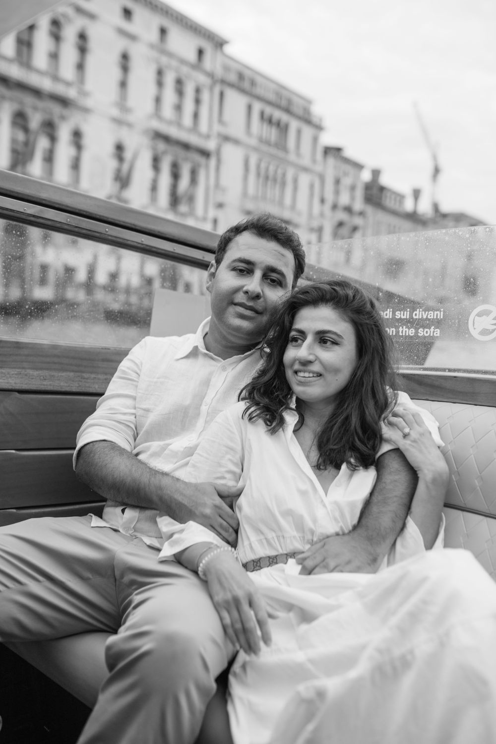 Couple relaxing in a classic Venetian boat against historic buildings in black and white.