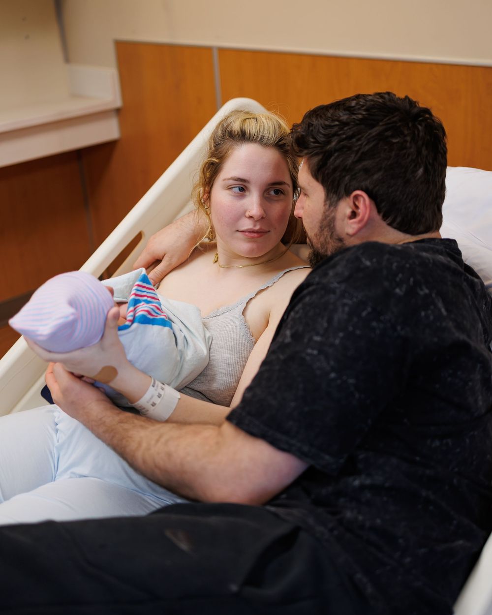 Two people share a tender moment as one holds a baby bottle while resting together in a hospital-like setting.