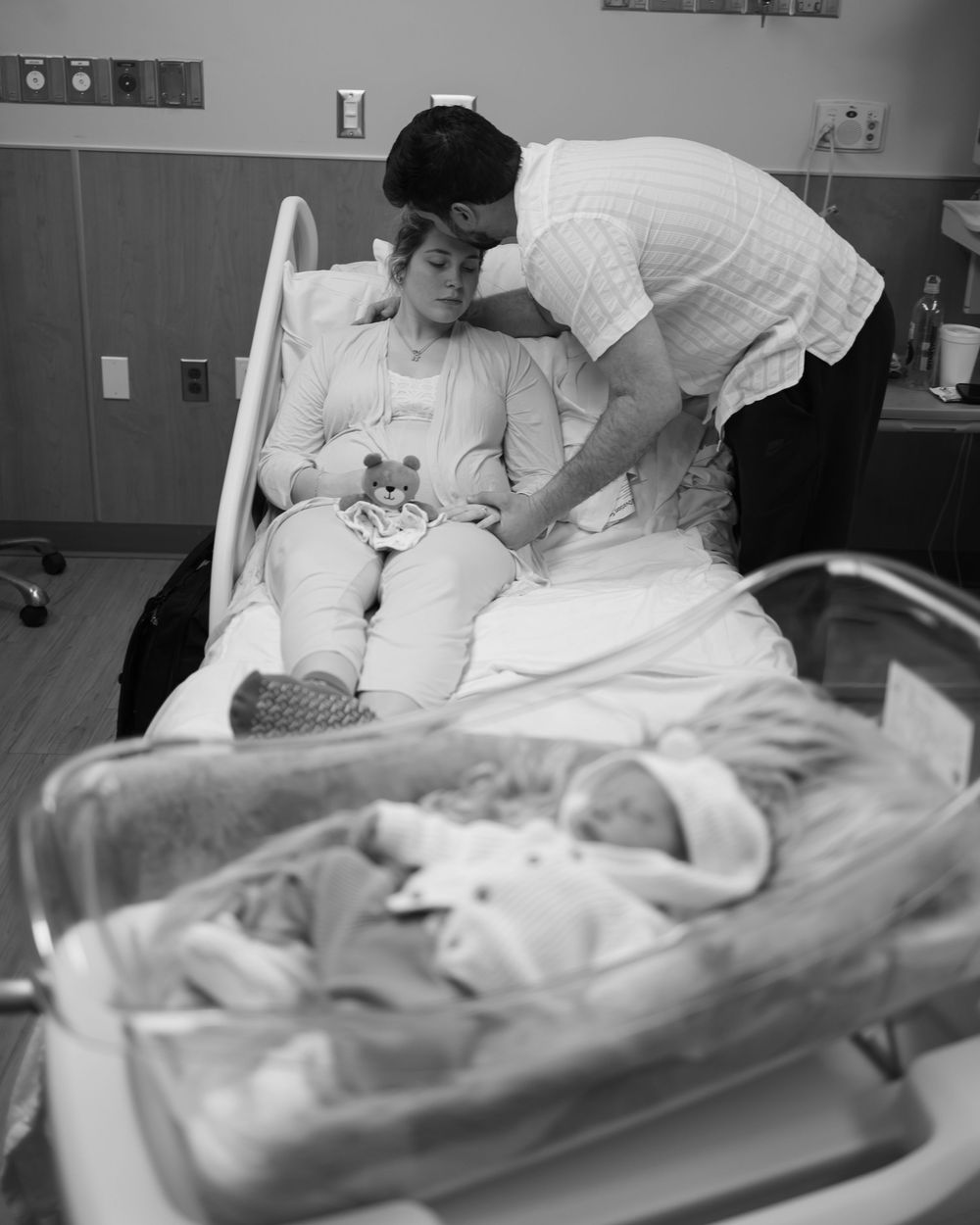 A vintage black and white hospital scene showing a patient in bed with someone attending to them beside a medical bassinet.