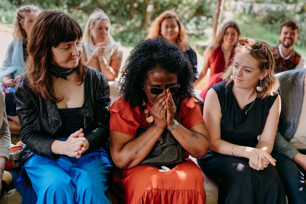 People sit together outdoors as someone in a red dress reacts emotionally among friends at a gathering.